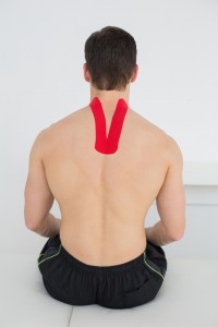 Rear view of a shirtless young man with red kinesio tape on back in the medical office
